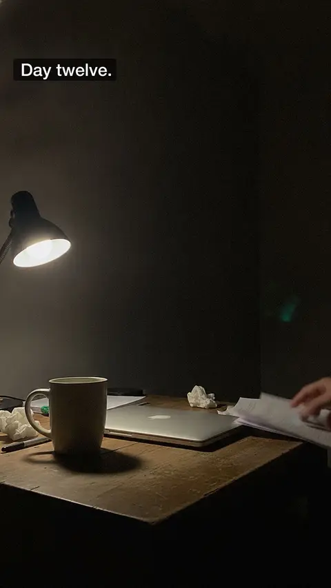 A lamp on a dark desk at night, captioned "Day twelve."